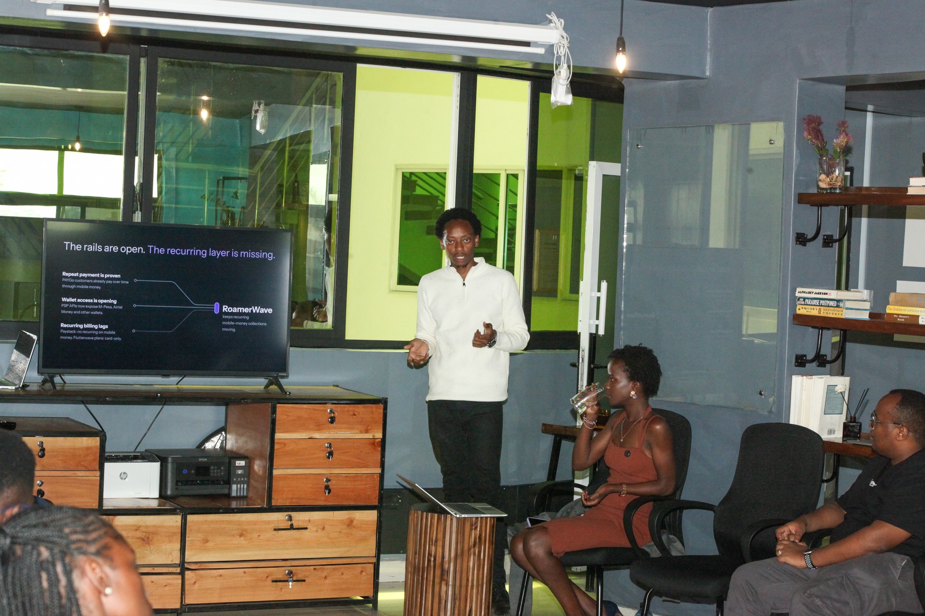 A presenter speaking to a seated group in a shared workroom