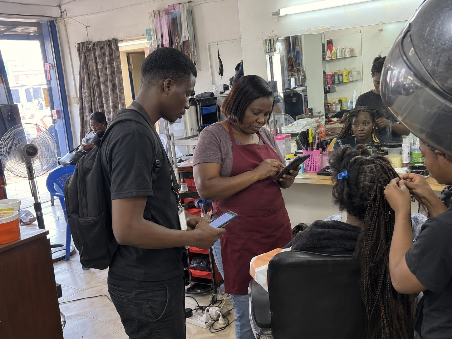 A salon owner paying a founder by mobile money while a client has her hair braided